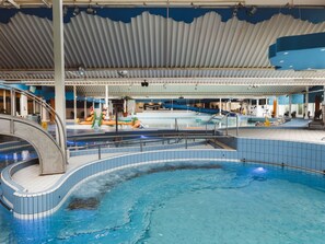Ein Hallenbad mit Rutsche, Kinderspielbereich und überdachter Sitzgelegenheit.