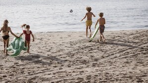 Ein sandiger Strand mit Fußabdrücken und einem Fußball in der Ferne.