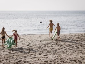 Ein sandiger Strand mit Fußabdrücken und einem Fußball in der Ferne.