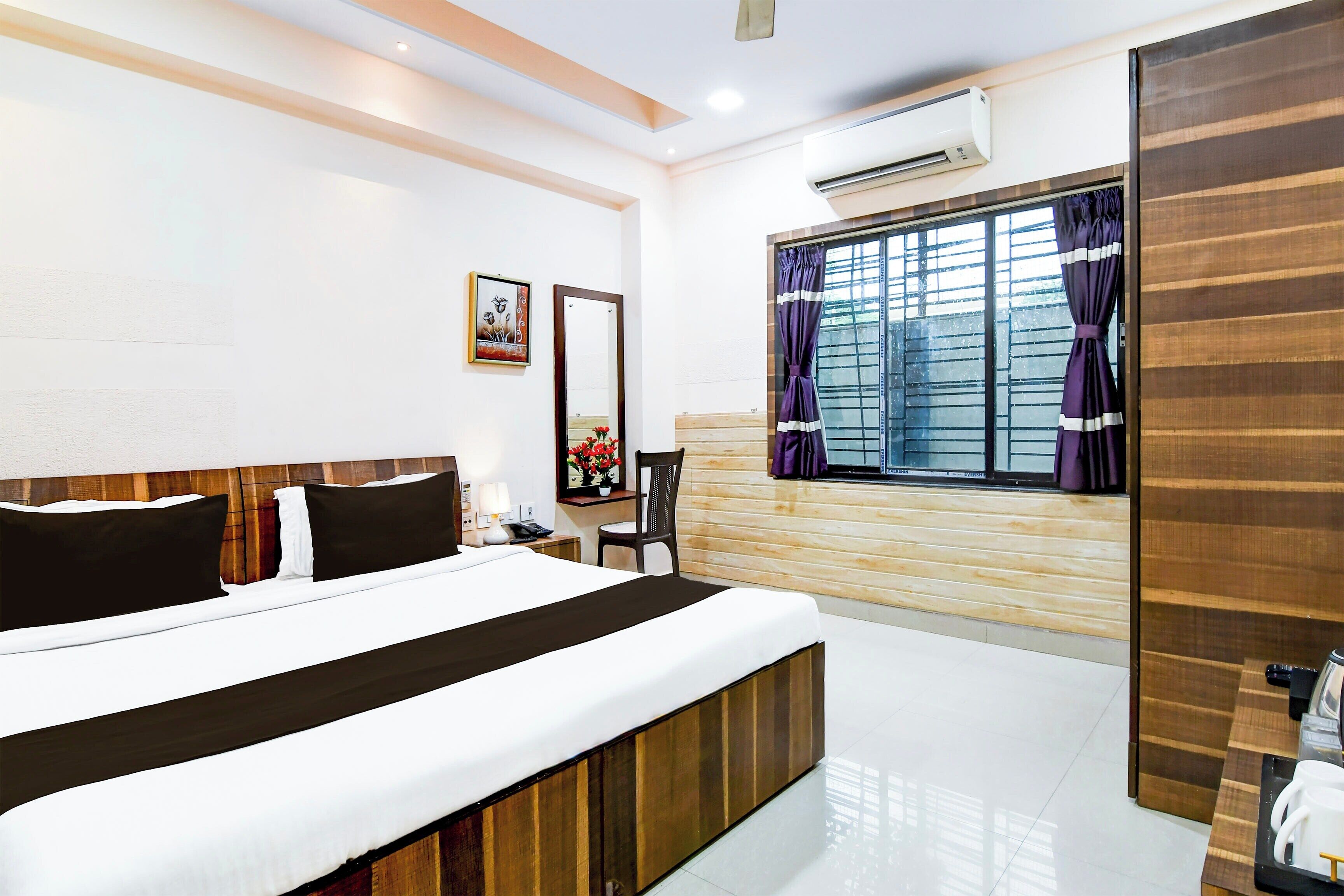 Habitación de hotel con cama, escritorio, silla, aire acondicionado y ventana con cortinas.