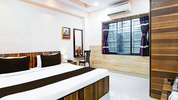 Habitación de hotel con cama, escritorio, silla, aire acondicionado y ventana con cortinas.