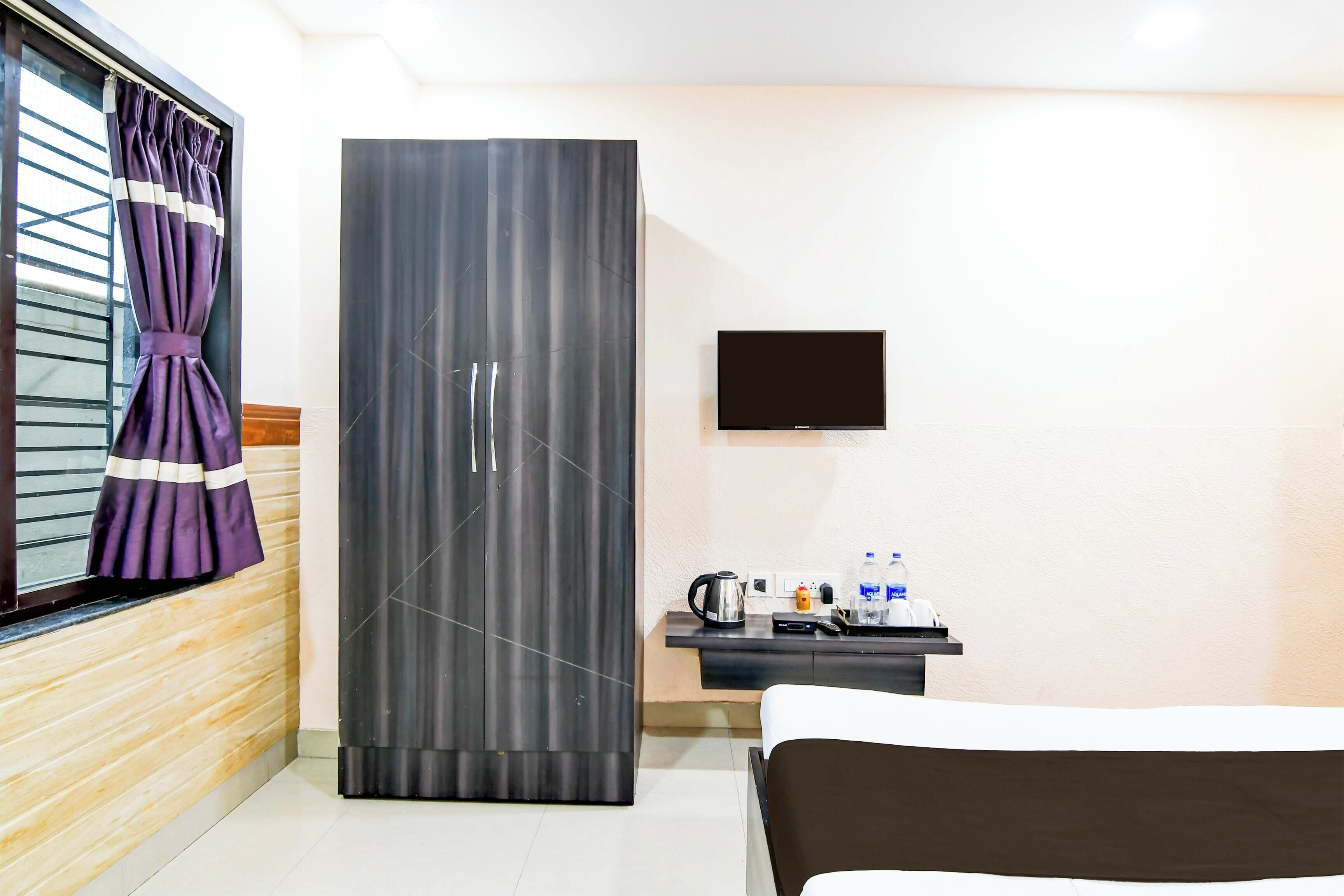Quarto de hotel com cama, guarda-roupa, secretária e televisão de ecrã plano, e janela com cortinas.