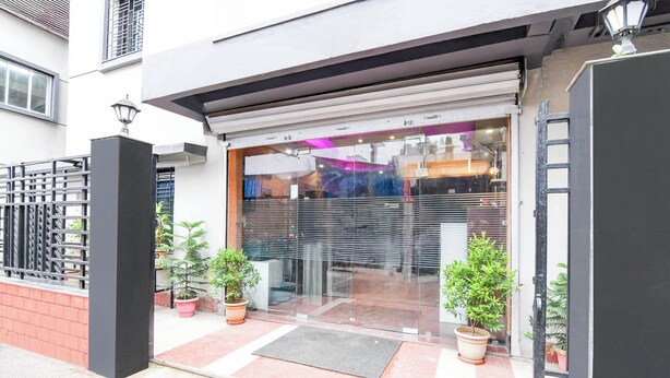 A building entrance with a glass door, potted plants, and a metal gate. - Super Collection O Behala (Alipur)