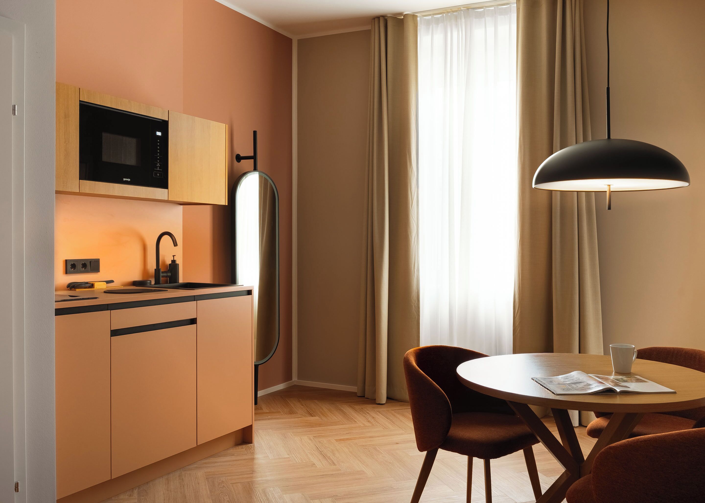 Une cuisine moderne équipée d’un four à micro-ondes, d’un évier et de placards, un coin repas avec une table et des chaises, et une grande fenêtre avec des rideaux.