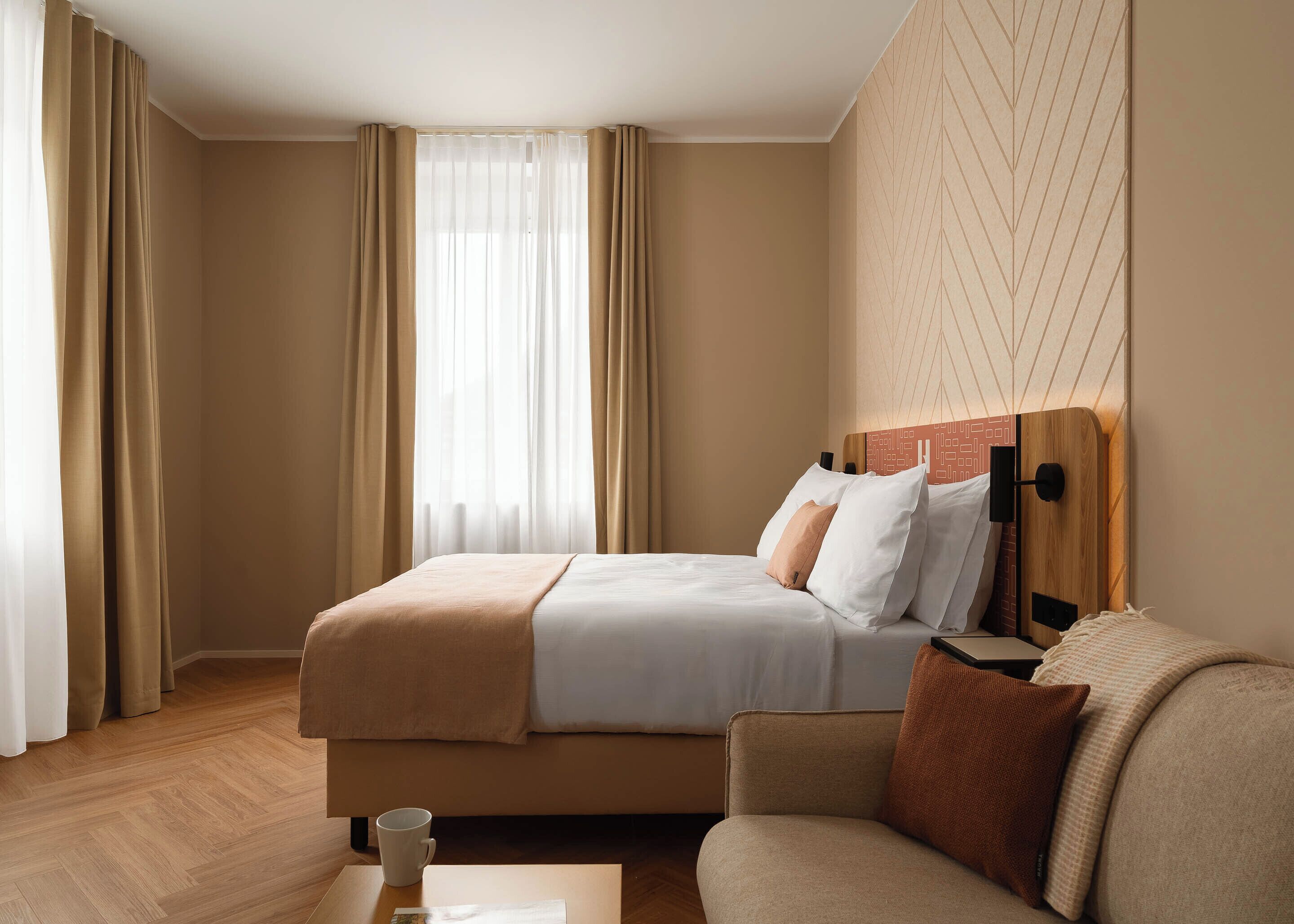 Una habitación de hotel con cama, sofá, una mesita de centro y una ventana con cortinas.