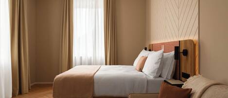 Una habitación de hotel con cama, sofá, una mesita de centro y una ventana con cortinas.