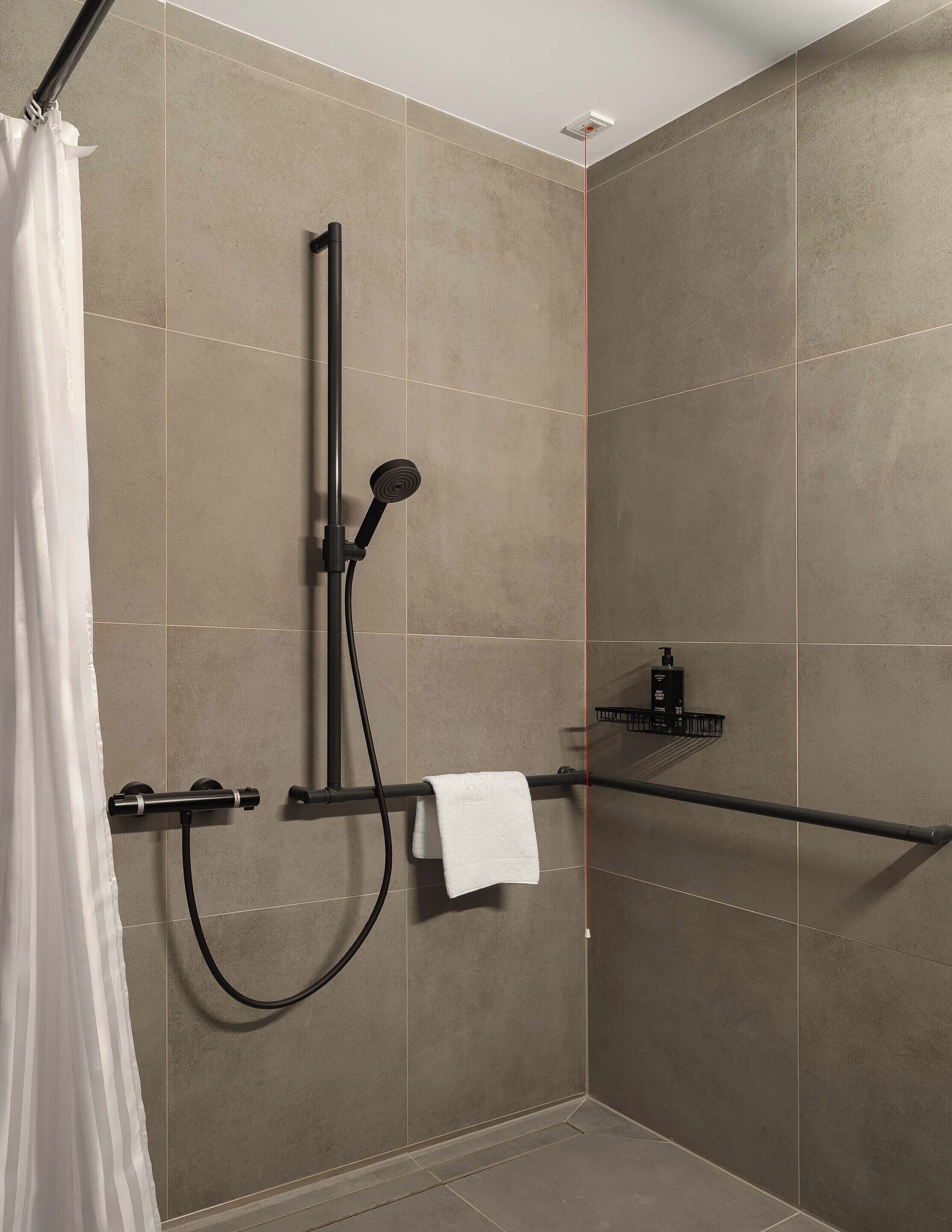 A shower area with a handheld showerhead, a towel rack, and a soap dispenser.