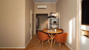 A modern dining area with a round table, four orange chairs, a pendant light, and a built-in shelf with kitchenware. - Limehome Linz Urfahr (Linz)