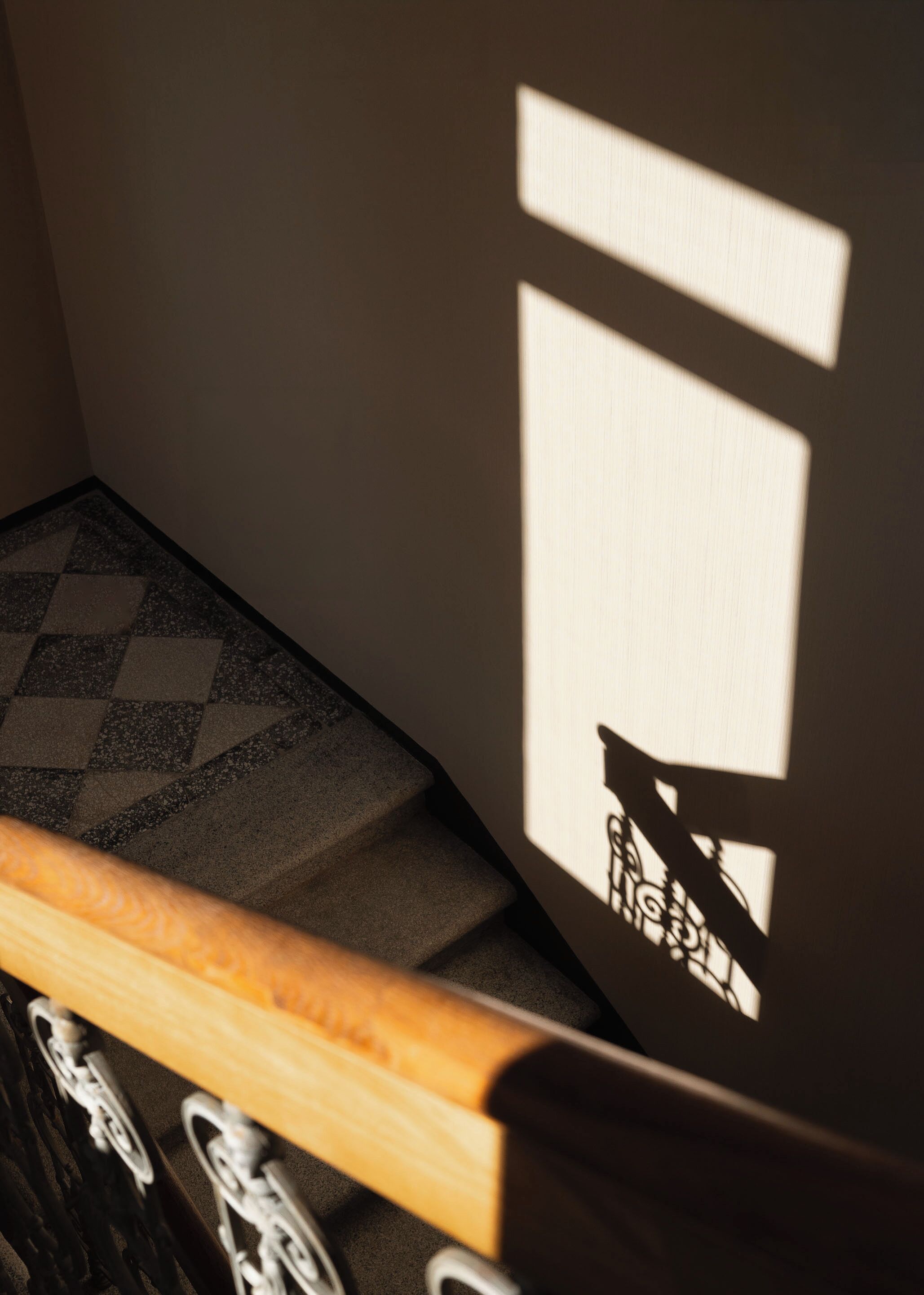 Een detail van een houten bank met metalen frame, een vloer met een patroon en een muur met een geometrische schaduw.