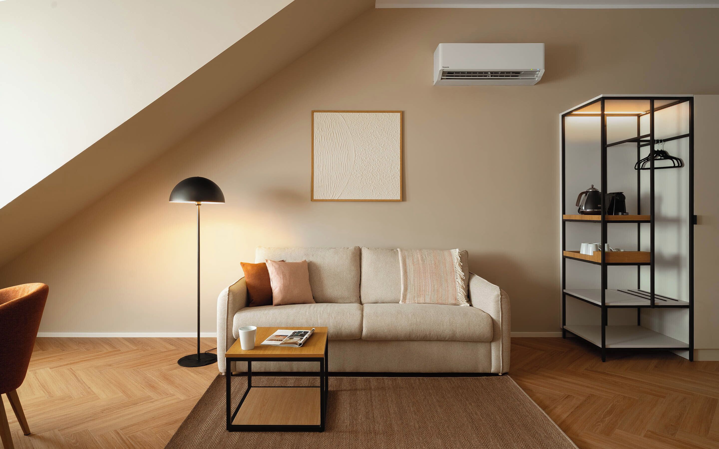 A modern living room with a sofa, a coffee table, a floor lamp, a wall-mounted air conditioner, and a shelving unit.