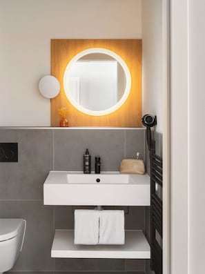 A modern bathroom with a white sink, a round mirror with a wooden frame, and a towel rack.