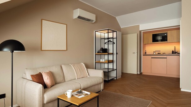 A modern living room with a sofa, a coffee table, a floor lamp, and a bookshelf. - Limehome Linz Urfahr (Linz)