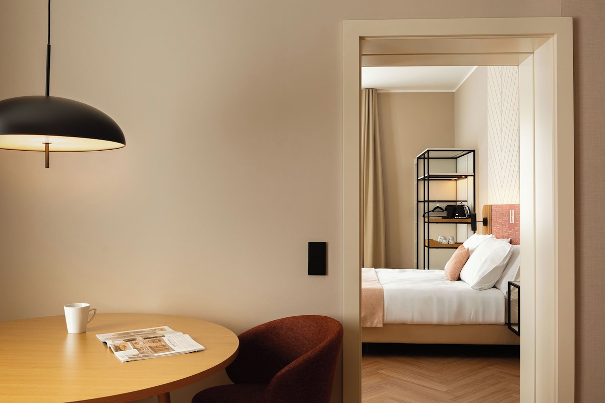 A hotel room with a bed, bedside table, and a reading area with a table and chair.