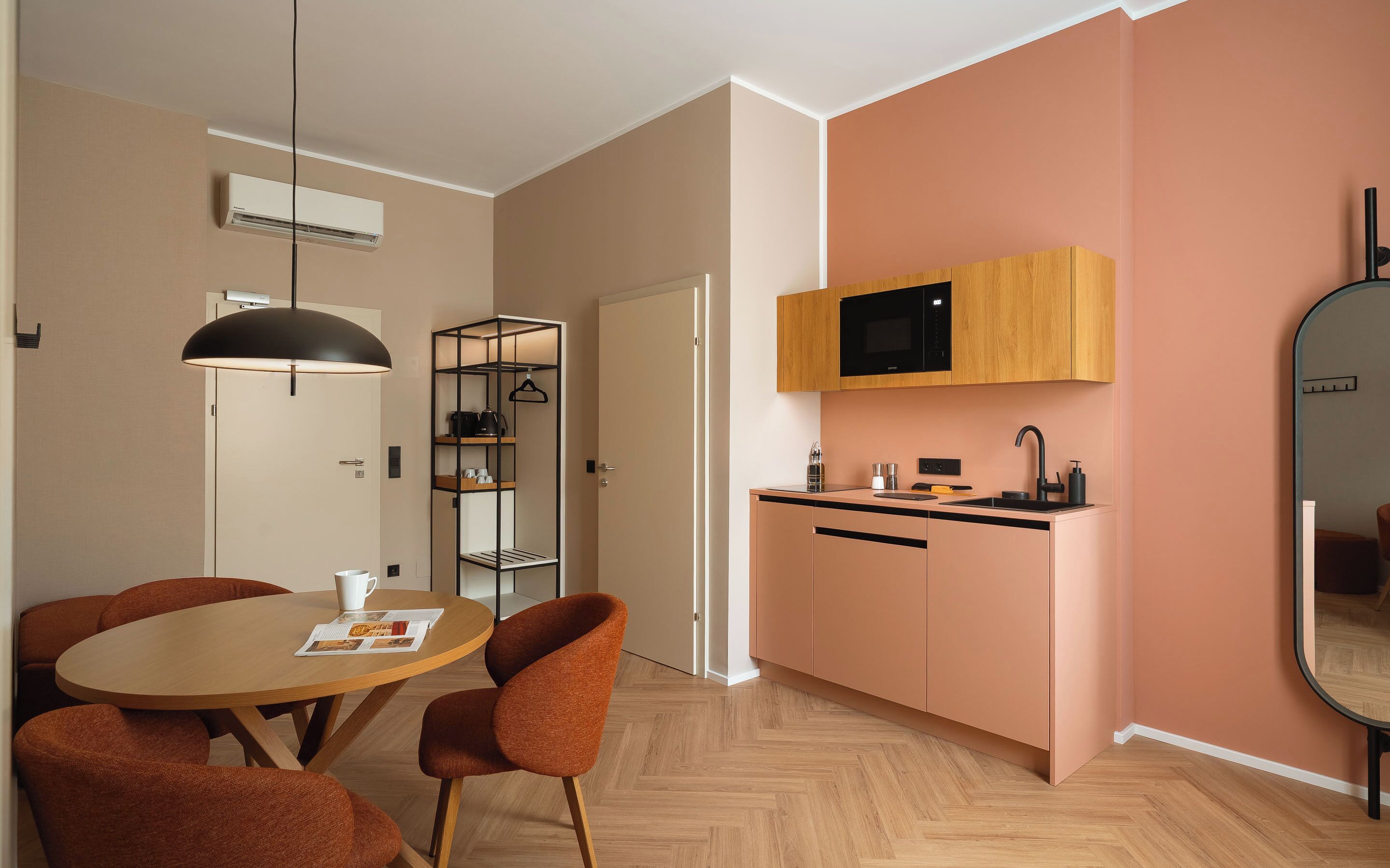 Eine moderne Küche mit Mikrowelle, Spüle und Holzschränken. Ein Essbereich mit einem runden Tisch und orangefarbenen Stühlen ist ebenfalls vorhanden.