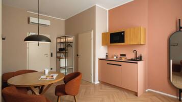 Eine moderne Küche mit Mikrowelle, Spüle und Holzschränken. Ein Essbereich mit einem runden Tisch und orangefarbenen Stühlen ist ebenfalls vorhanden.