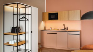 A compact kitchenette with a microwave, sink, and wooden cabinets. - Limehome Linz Urfahr (Linz)
