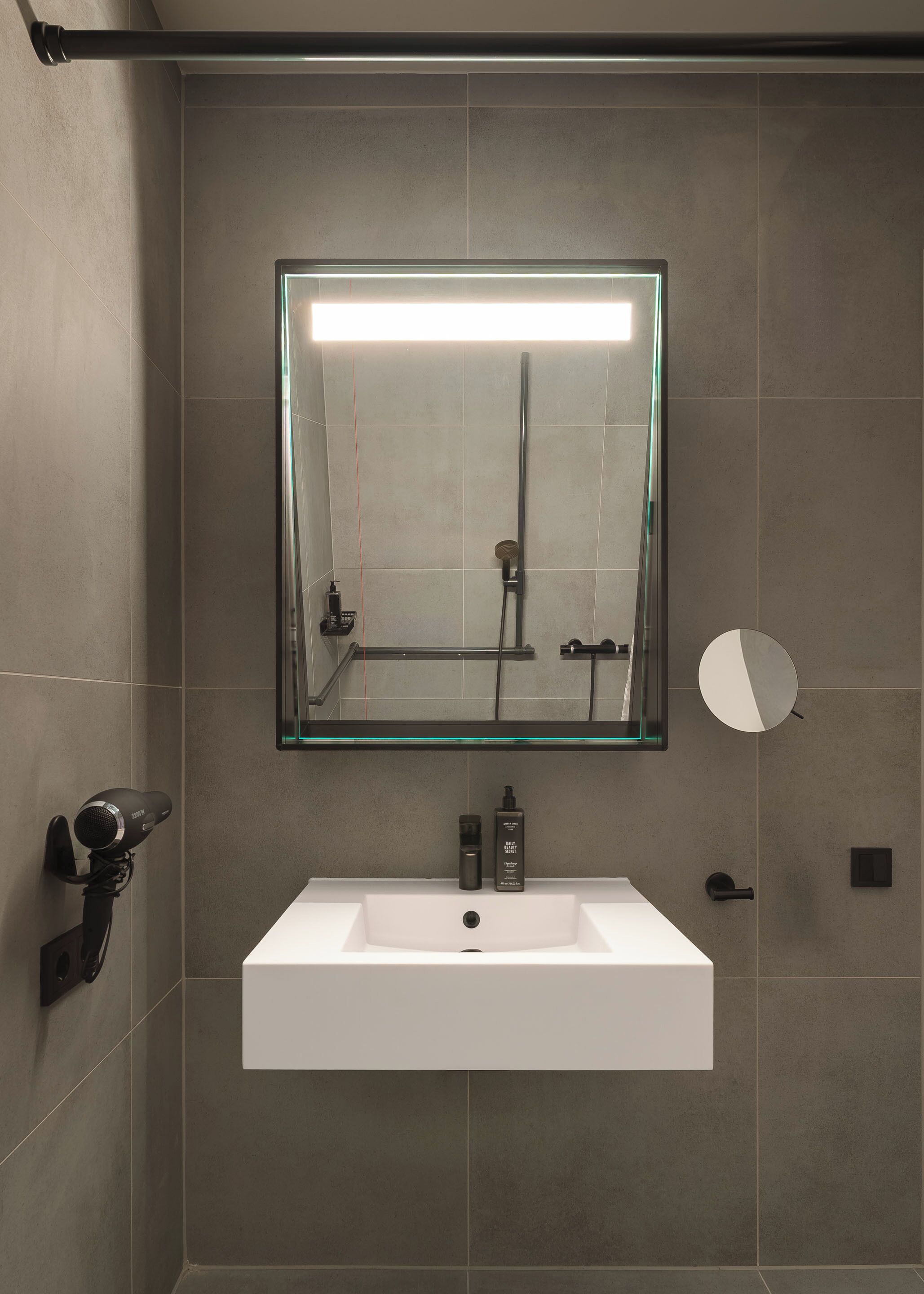 Une salle de bain avec un lavabo blanc, un miroir, un sèche-cheveux et une pomme de douche.