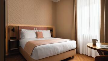 Habitación de hotel con cama, mesitas de noche, televisor montado en la pared y ventana con cortinas.