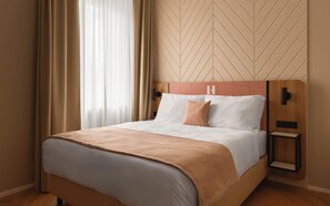 Ett hotellrum med en säng, ett nattduksbord och en vägg med ett geometriskt mönster.
