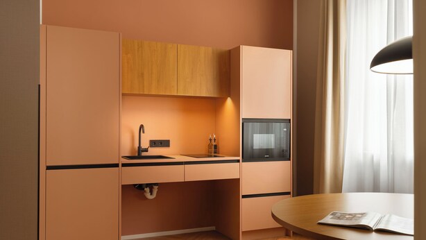 Una cocina compacta con microondas integrado, un lavamanos y armarios de madera.