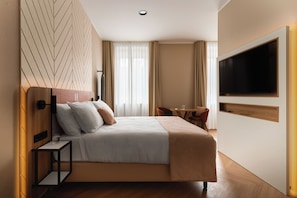 A modern hotel room with a large bed, a TV mounted on the wall, and a small table with chairs.