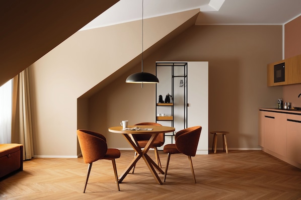 A modern kitchen with a dining area, wooden flooring, and a black pendant light.