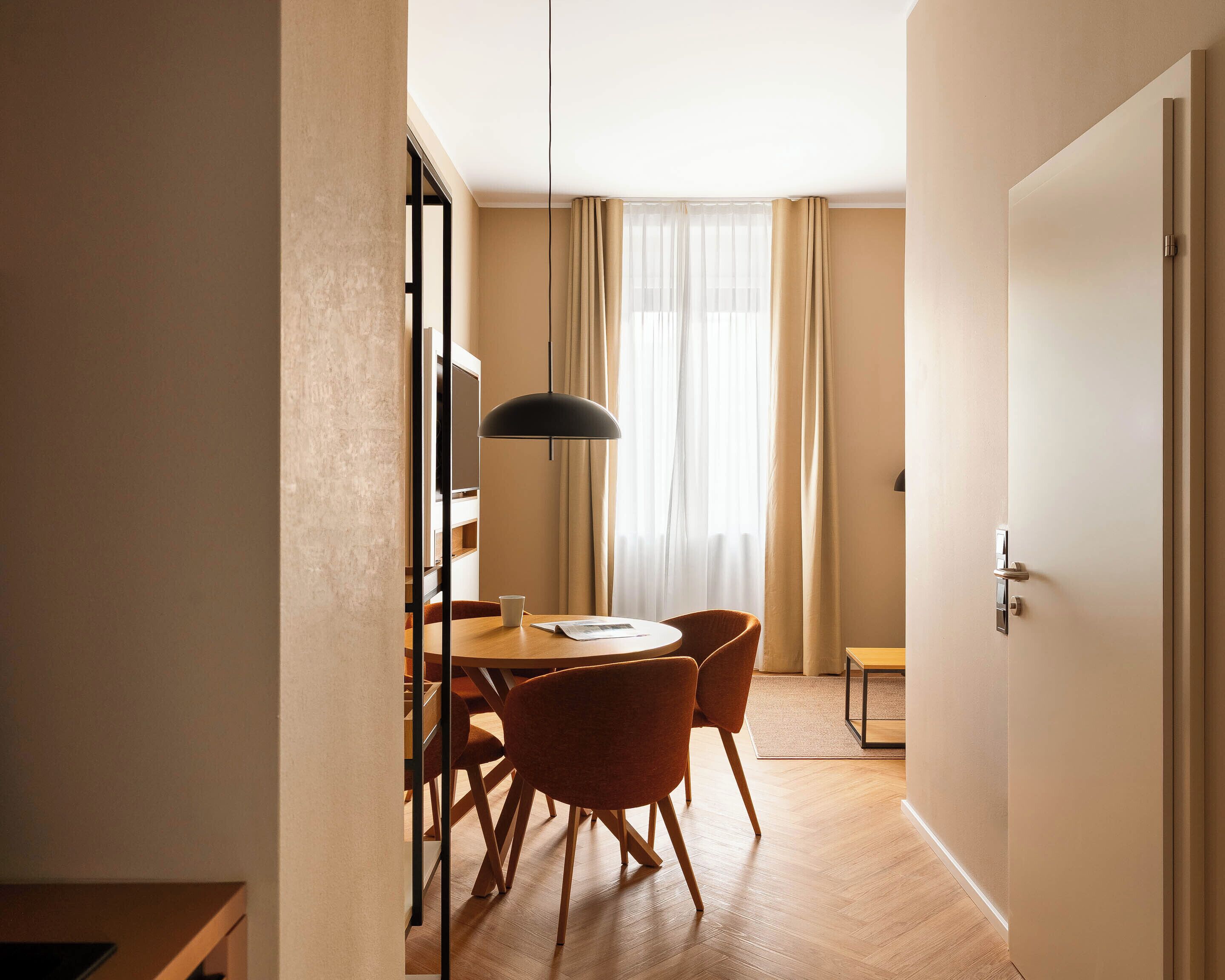 Ein Hotelzimmer mit Essbereich, ausgestattet mit einem runden Tisch, Stühlen und einer Pendelleuchte.