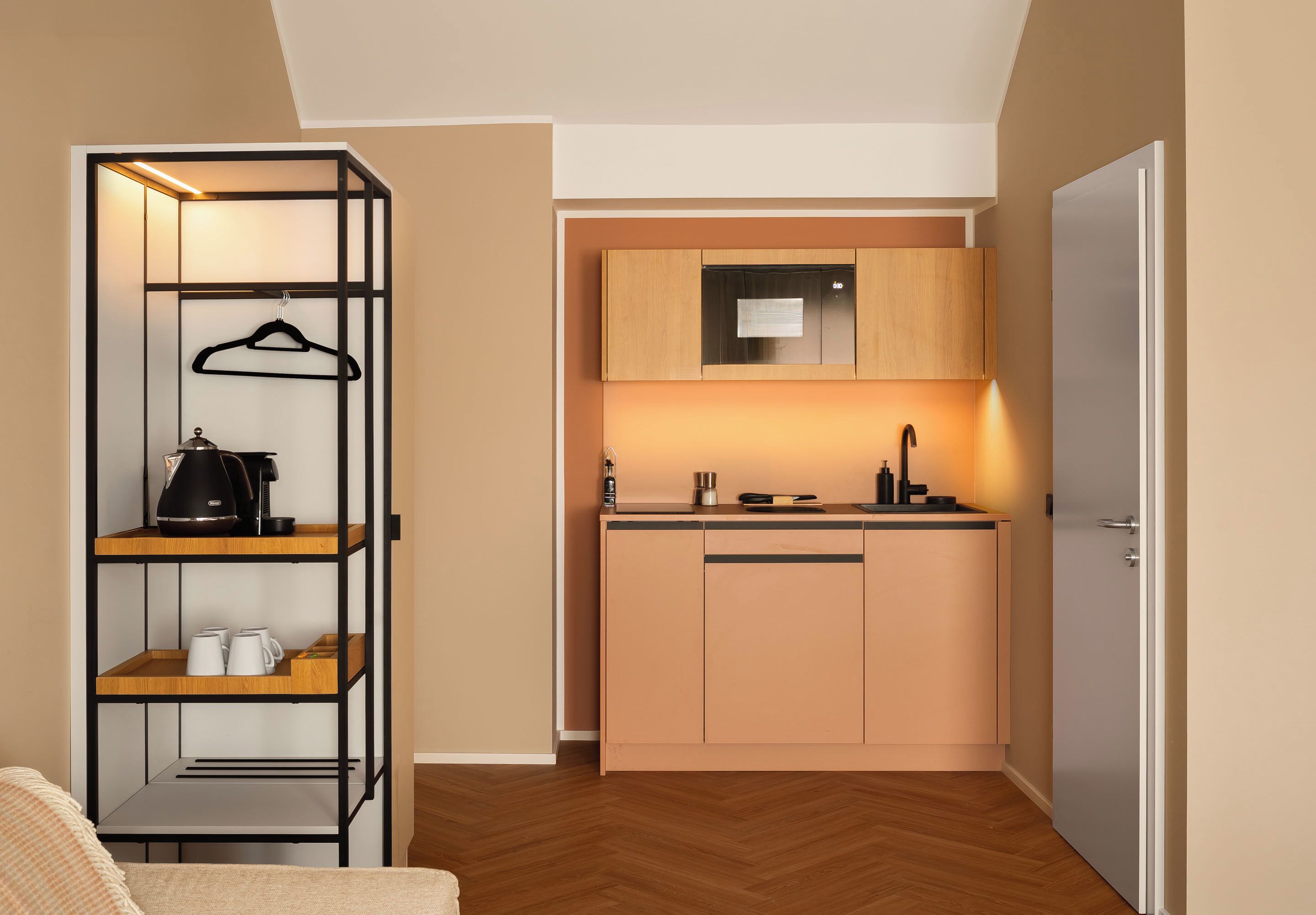 A compact kitchen with a built-in oven, a coffee machine, and a hanging rack.