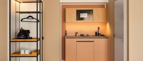 A compact kitchen with a built-in oven, a coffee machine, and a hanging rack.