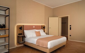 A hotel room with a bed, a nightstand, a shelf with items, and a door leading to another room.
