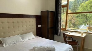 A hotel room with a bed, a desk, and a view of a forested area.
