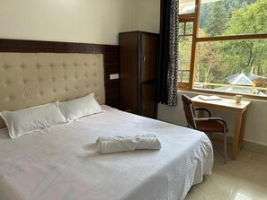 A hotel room with a bed, a desk, and a view of a forested area.