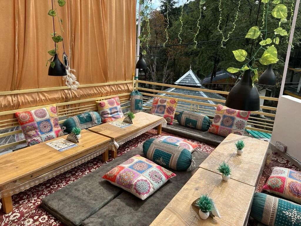 A cozy outdoor seating area with cushioned benches and tables, adorned with colorful cushions and small potted plants.