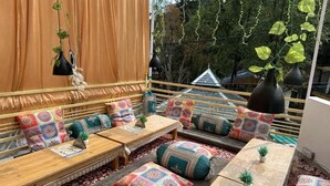 A cozy outdoor seating area with cushioned benches and tables, adorned with colorful cushions and small potted plants.