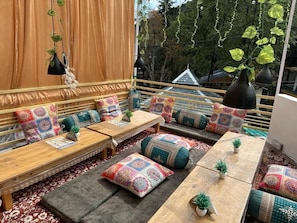 A cozy outdoor seating area with cushioned benches and tables, adorned with colorful cushions and small potted plants.