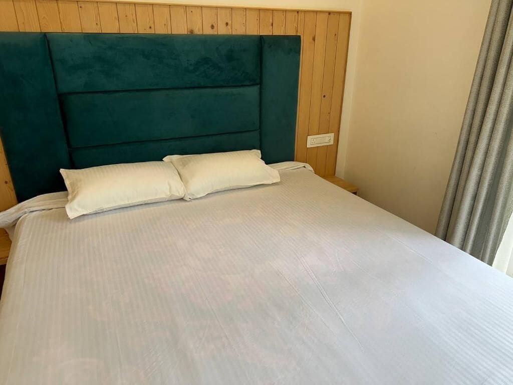 Una cama con cabecera color turquesa y ropa de cama blanca en una habitación con paneles de madera.