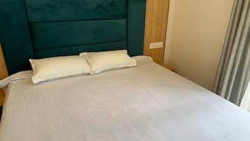 Una cama con cabecera color turquesa y ropa de cama blanca en una habitación con paneles de madera.