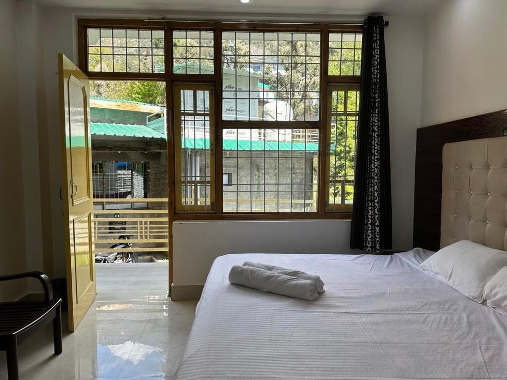 A hotel room with a bed, a bench, and a large window with a view of the outside.