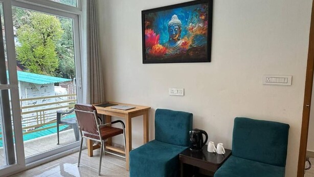 A room with a desk, two teal chairs, a painting, and a view through a glass door.