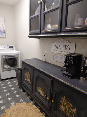 Una cocina con lavadora y secadora integradas, cafetera y un letrero que dice 'PANTRY bake cook create'.