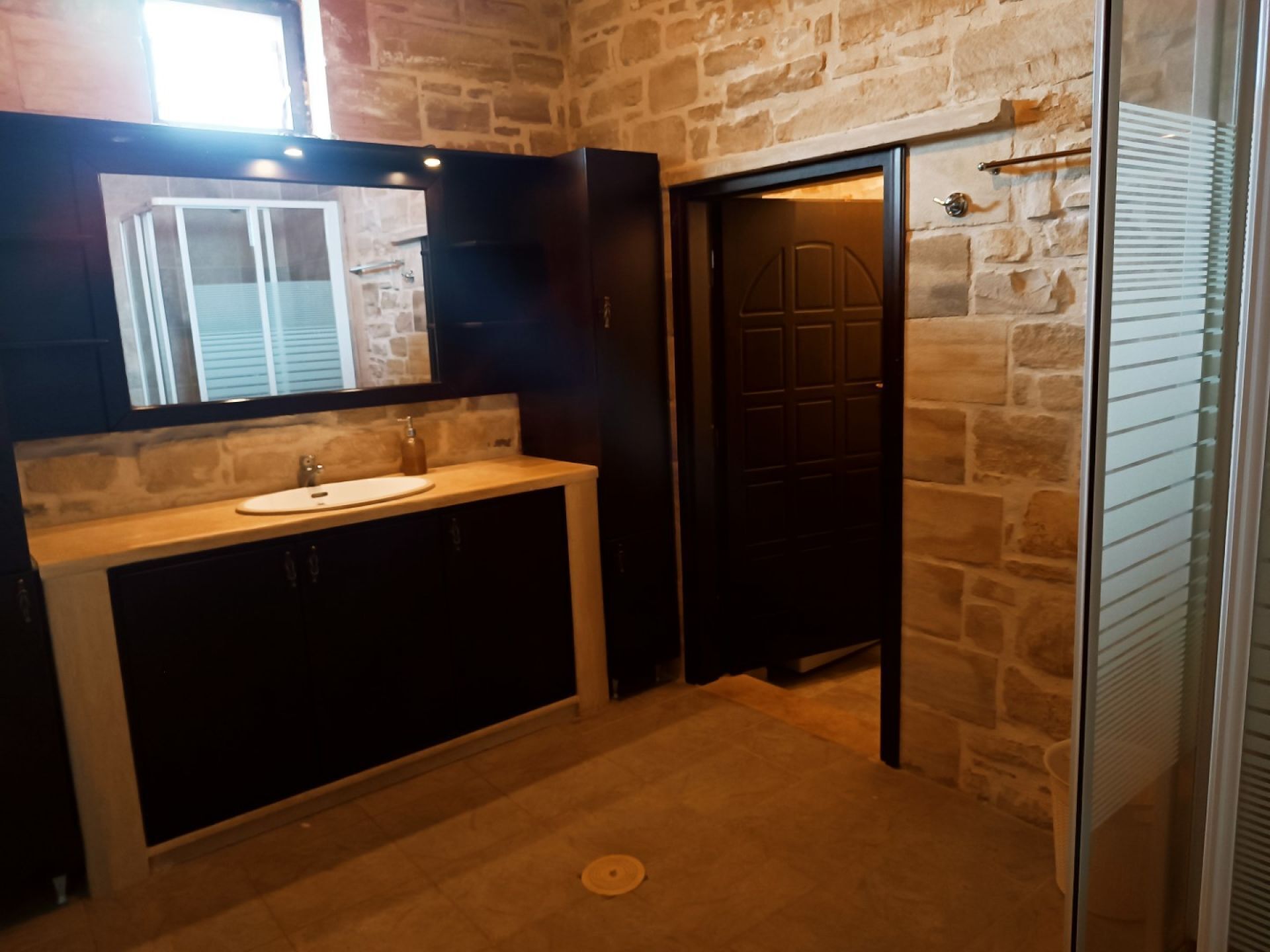 Un baño con pared de piedra, un lavamanos y una puerta.