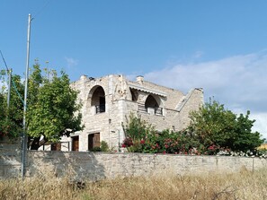 Edificio de piedra con dos ventanas arqueadas y un muro de piedra frontal.