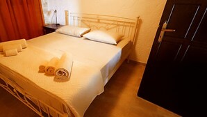 A bed with white linens and rolled towels, a bedside table with a lamp, and a door to the right.
