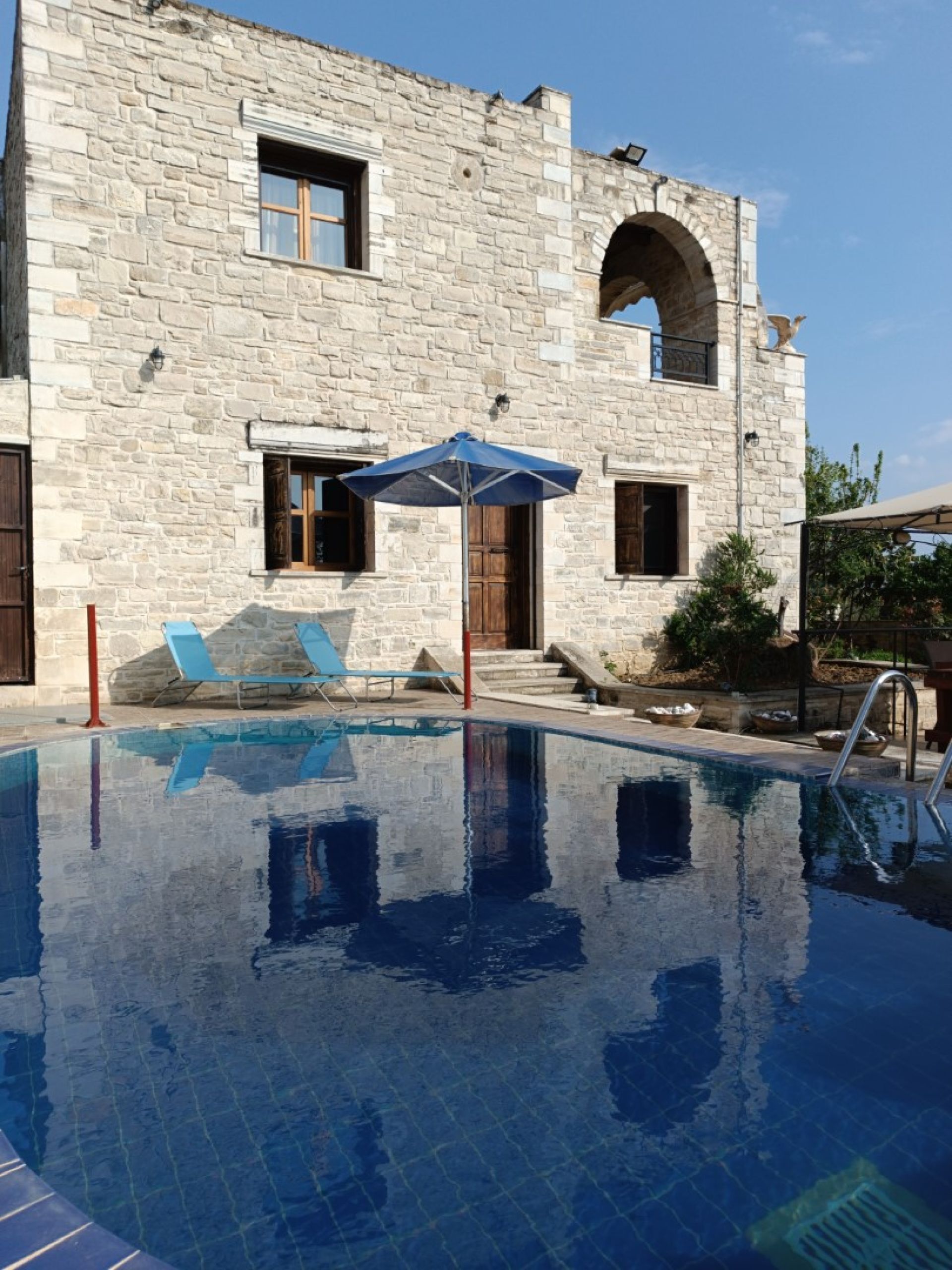 Un edificio de piedra con piscina, una sombrilla azul y una escalera metálica que da a la piscina.