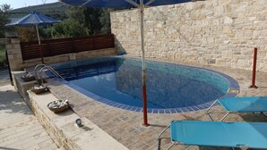 A swimming pool with a stone wall, a wooden fence, and a blue umbrella.