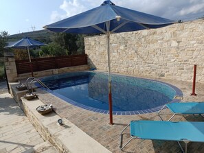 A swimming pool with a stone wall, a wooden fence, and a blue umbrella.