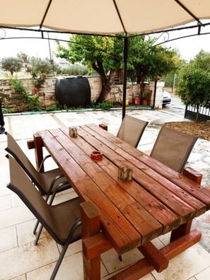 Un patio al aire libre con una mesa y sillas de madera, un gran paraguas y un muro de piedra con plantas.