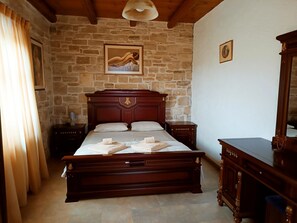 Un dormitorio con pared de piedra, cama de madera, dos mesitas de noche, un espejo y un cuadro en la pared.