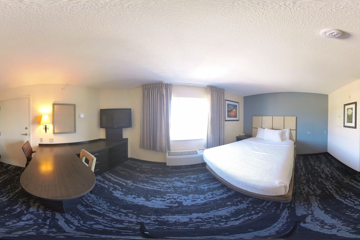 Une chambre d’hôtel avec un lit, un bureau, une télévision et une fenêtre avec des rideaux.