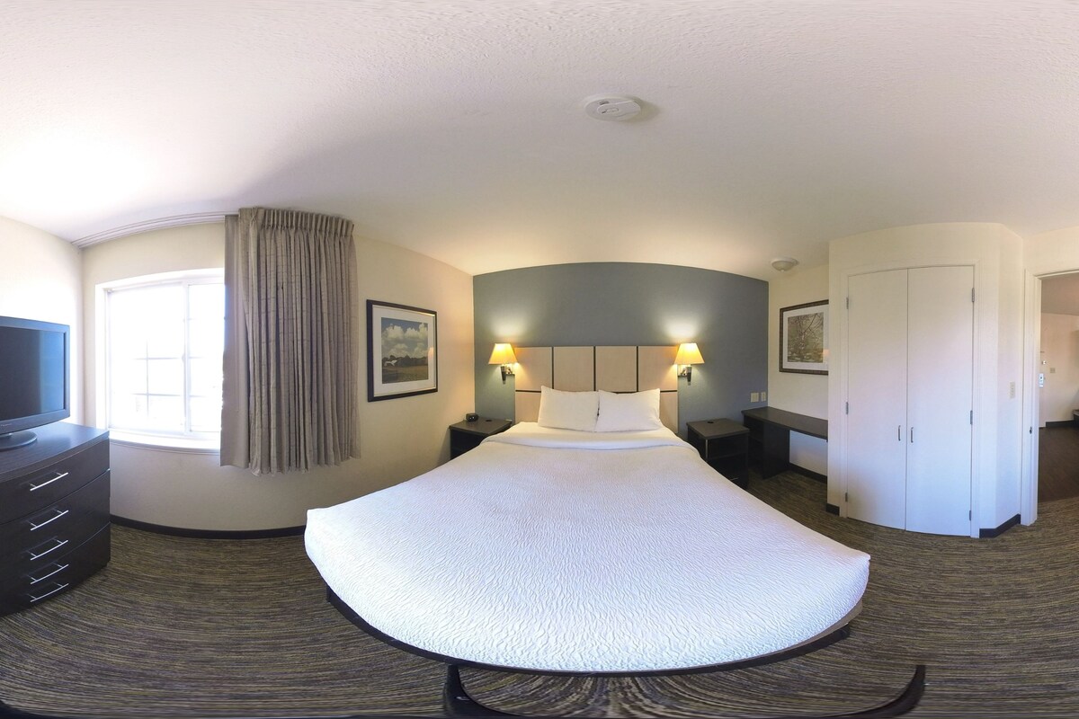 Une chambre d’hôtel avec un lit à la forme arrondie, une télévision, un bureau et une armoire.
